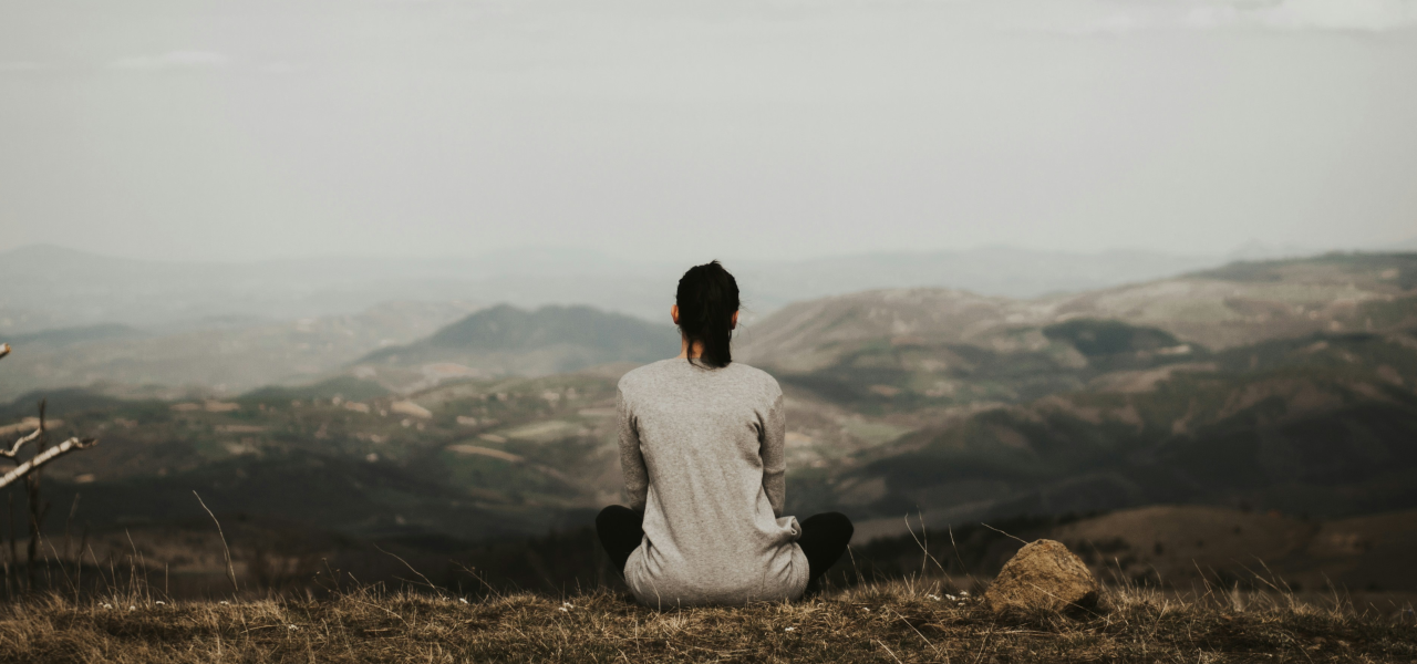 Wissensbeitrag: Burnout-Prävention: Tipps gegen das Ausbrennen, Frau sitzt auf Berg und schaut in die Landschaft
