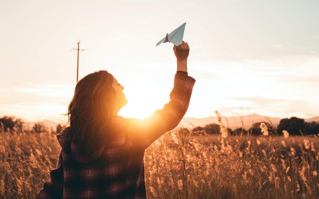 Zuversicht - Frau mit Papierflieger bei Sonnenuntergang