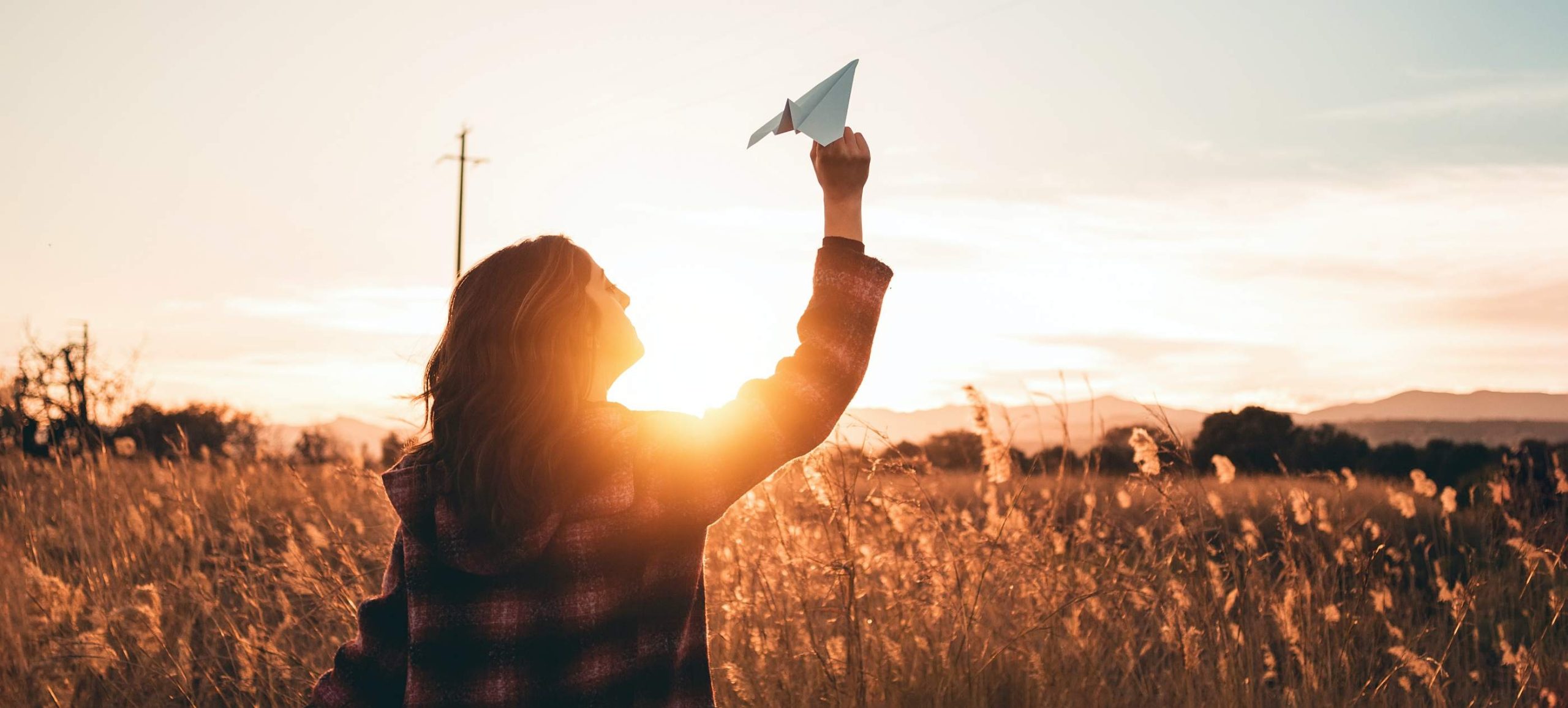Zuversicht - Frau mit Papierflieger bei Sonnenuntergang am Feld