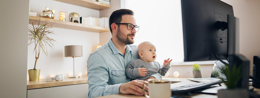 Mann mit Baby im Arm an einem Computer