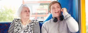 Im Bus telefoniert ein junger Mann laut. Eine alte Dame, die neben ihm sitzt, schaut ihn schockiert an.