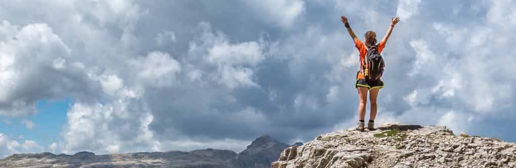 Eine Frau steht auf einem hohen Berg und hat die Arme nach oben ausgestreckt.