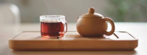 Eine Tasse Tee und eine Teekanne stehen auf einem Holztablett.