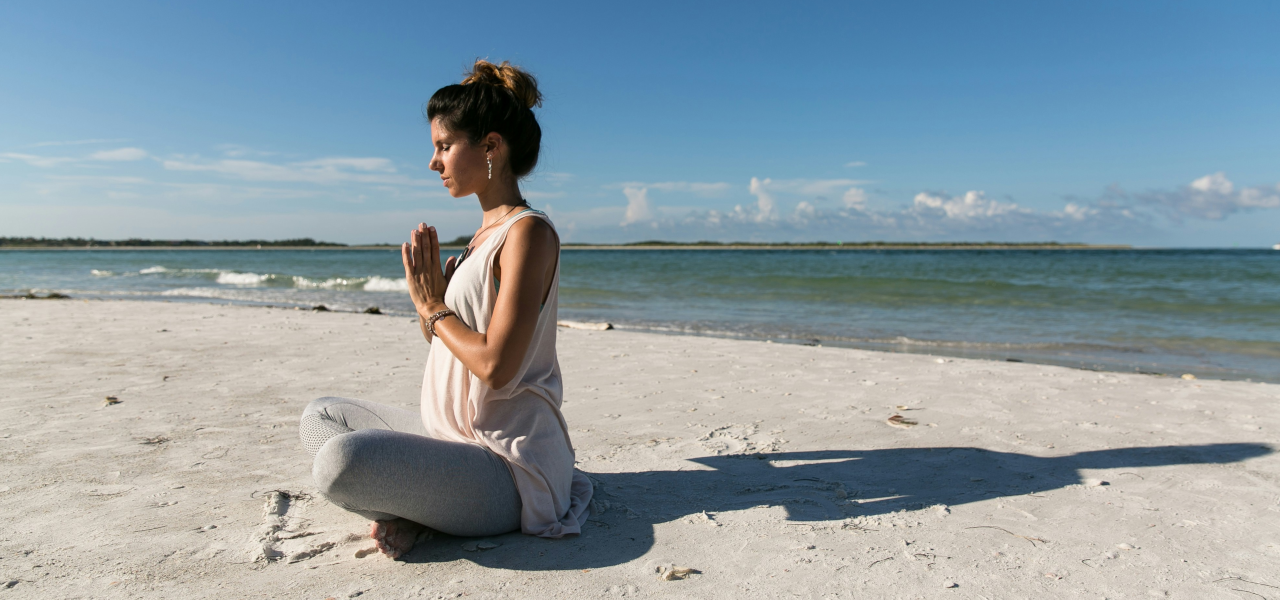 Meditieren für Anfänger, Frau sitzt am Strand und meditiert, geführte Meditation