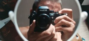 Ein Mann fotografiert sich mit einer Spiegelreflexkamera in einem kleinen runden Spiegel.