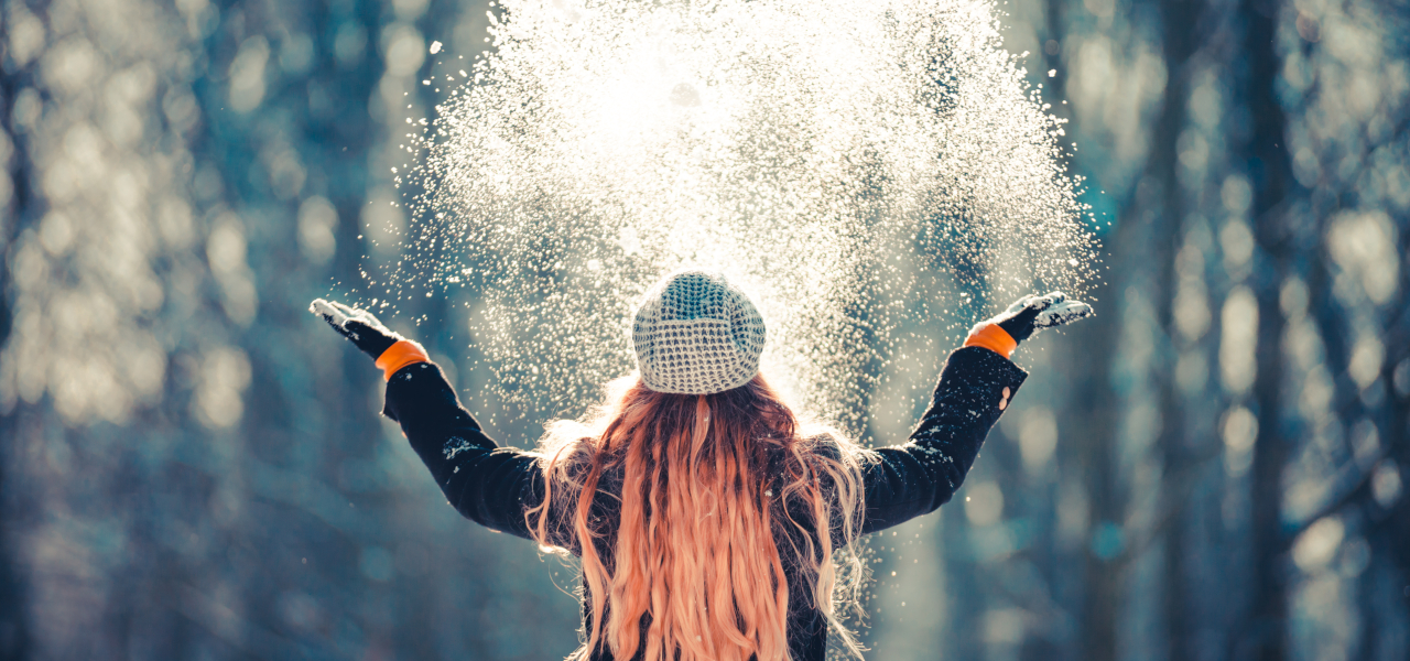 Frau steht in Winterlandschaft und wirft Schnee in die Luft